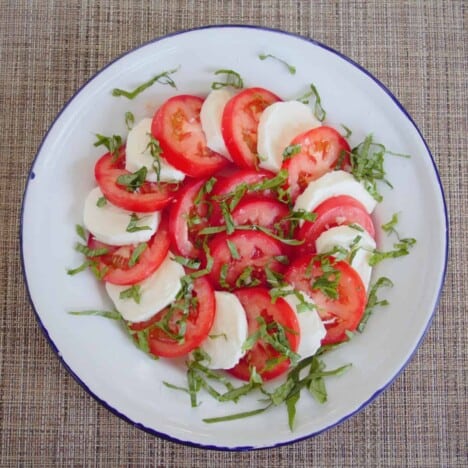 Looking down onto a pinwheel of sliced tomatoes and mozzarella sprinkled with basil.