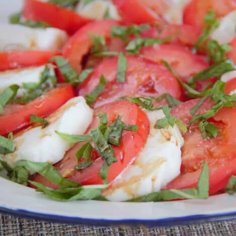 A close up of a plate of sliced tomatoes and mozzarella, sprinkled with basil.