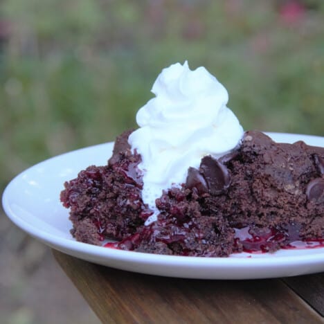 A white plate with a serving of cherry chocolate dump cake topped with whipped cream.