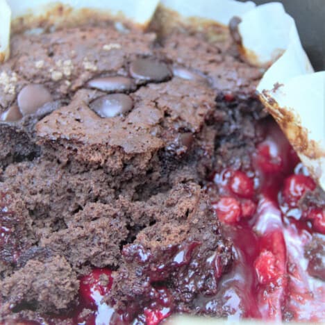 Cooked chocolate dump cake partly served, exposing the cherry mixture below.
