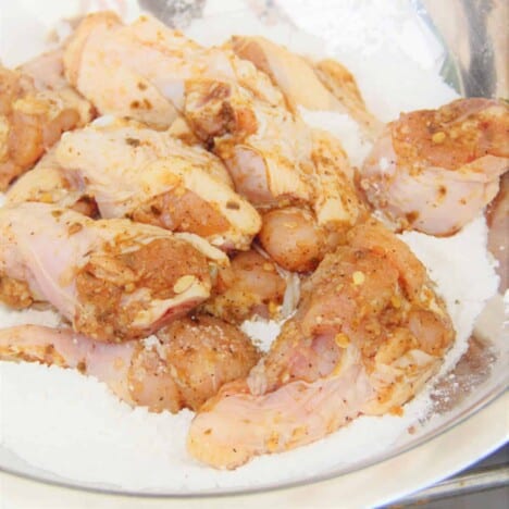 Marinated chicken wings tossed in rice flour in a large stainless steel bowl.