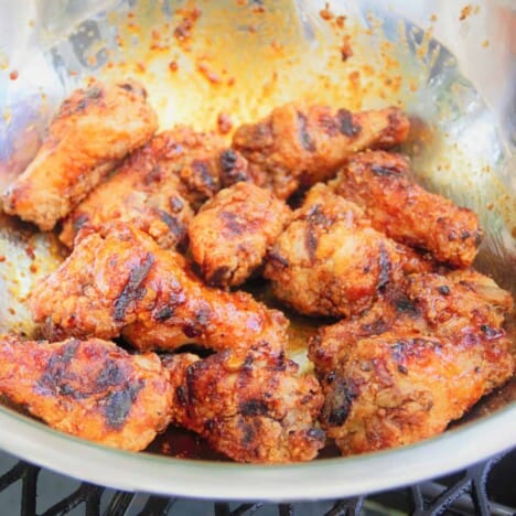Grilled chicken wings toss in barbecue sauce in a stainless steel bowl.