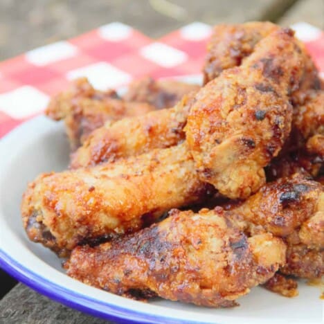 A white plate of golden brown crispy chicken wings on a red checkered tablecloth.
