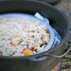 An unbaked peach crisp in a pie tin in a Dutch oven.