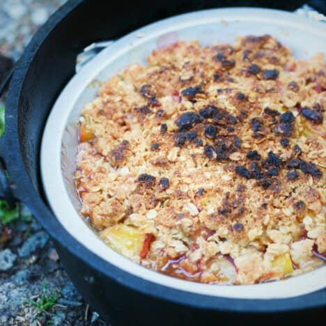 A cooked peach crisp in a pie tin in a Dutch oven.