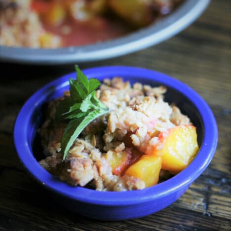 A serving of peach crisp is in a small blue bowl, garnished with mint.