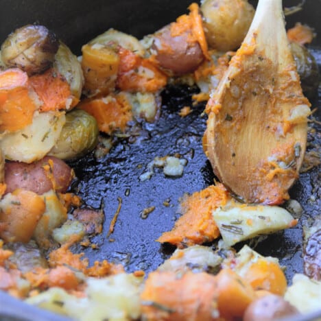 The Dutch oven baked vegetables being served with a wooden spoon.