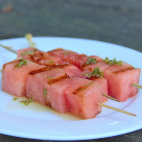 Grilled watermelon skewers on a white plate, served with a fruit dressing.