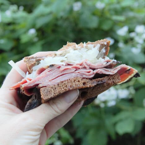 A halved reuben sandwich, exposing the fillings, is held up in the air.