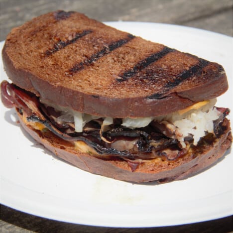 A grilled reuben sandwich sits on a white plate.