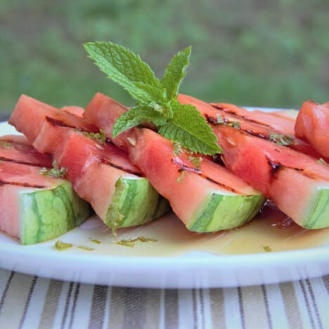 Wedges of grilled watermelon on a plate, drizzled with sauce and topped with fresh mint.