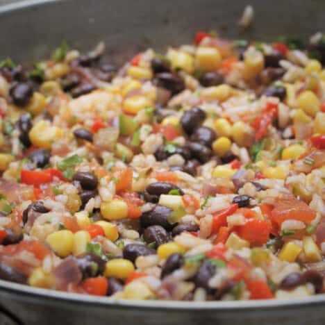 Close up in a frypan of a colorful mixture containing corn bits, black beans, red bell pepper and more.
