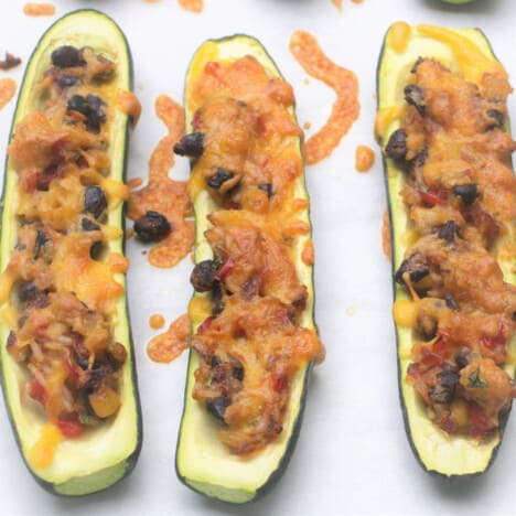 Three cooked stuffed zucchini sitting on a paper lined baking tray.