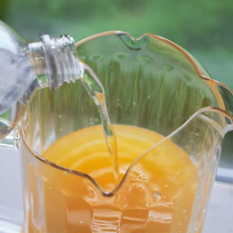 A plastic jug with pineapple juice having soda poured in.