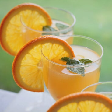 A set of glasses filled with pineapple orange mocktail garnished with orange slices and mint leaves.