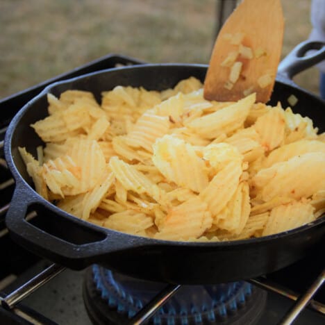 Potato chips being stirred in a skillet with a wooden spoon.