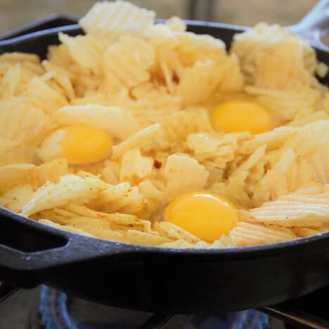 Three raw eggs in the potato chip hash in the skillet.