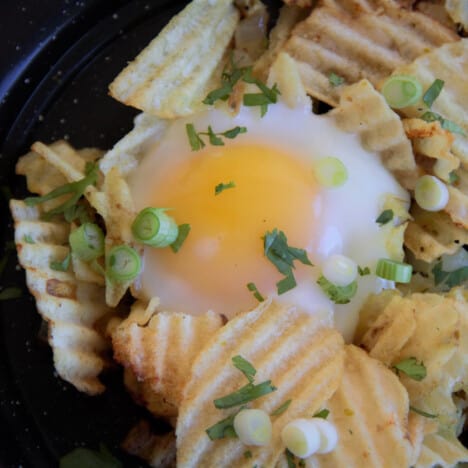 A close-up of the egg in the potato chip hash garnished with diced cilantro and slice green onion.