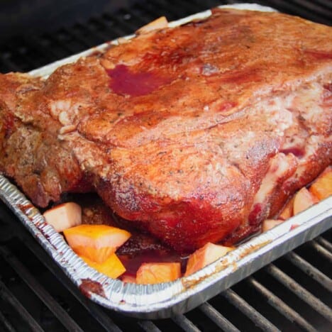 A smoked pork butt surrounded by the sangria fruit, in a half pan on the grill.