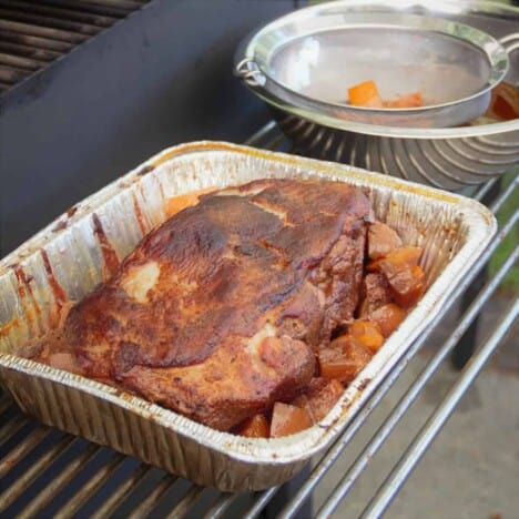 A smoked pork butt in a half pan with chunks of the sangria fruit.