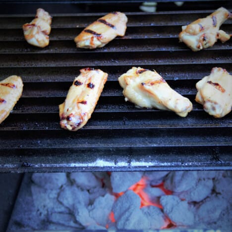 Chicken wings cooking on a grill grate over hot coals.