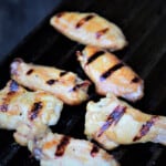 Glazed chicken wings are on a grill.