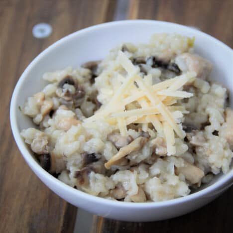 Looking down into a white bowl with a serving of chicken and mushroom risotto and topped with Parmesan cheese.