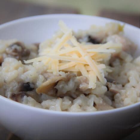 A close up of a serving of chicken and mushroom risotto topped with Parmesan cheese in a white bowl.