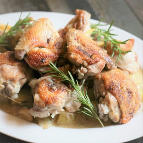 A white serving platter piled with browned chicken pieces and fresh rosemary.