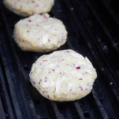 Three freshly made crab cakes having just being added to the grill to cook.