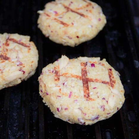 Three crab cakes on the grill with crossing grill lines on the top.