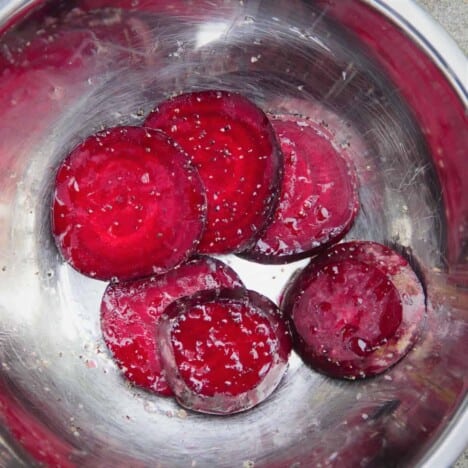 Sliced beets in a stainless steel bowl tossed with oil, salt, and pepper.