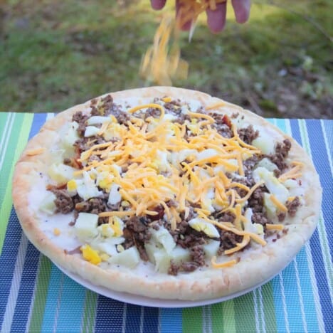 The shredded cheese being sprinkled over the breakfast pizza.