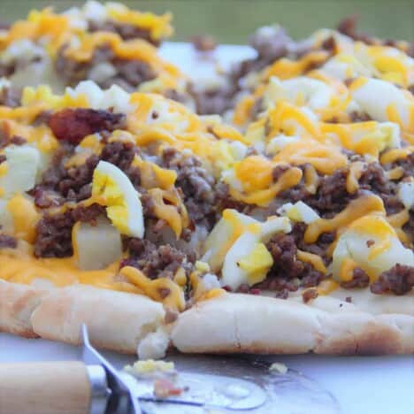 A full yet cut breakfast pizza sitting on a chopping board with the pizza cutter sitting in front of it.