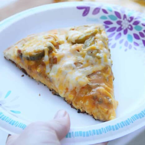 A slice of grilled cheeseburger pizza sits on a paper plate.