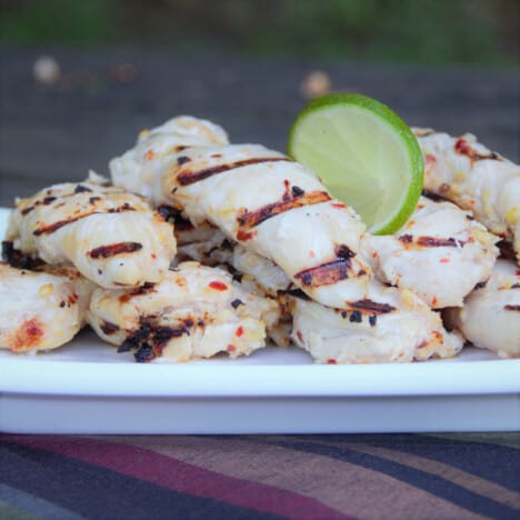 A plate of marinated and grilled chicken tenders with a lime slice.