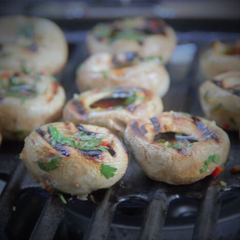 Medium mushrooms with strong grill marks and fresh cilantro and red pepper flakes on a grill.