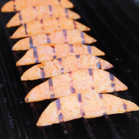 A row of charred sweet potato wedges are lined up on a grill.