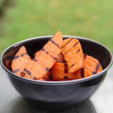 A black camping bowl holds a pile of grilled sweet potato wedges.