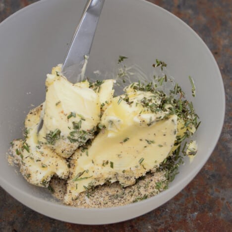 A plastic bowl with fresh herbs partly stirred through soft butter.