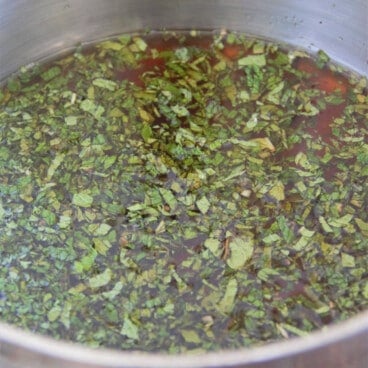 Finely diced green mint floating on a liquid in a saucepan.