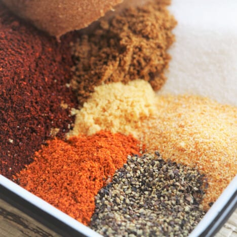 close up of a variety of herbs and spices with a focus on the pepper, garlic granules, and cayenne powder.
