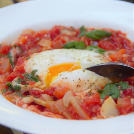 Close up of a poached egg in a tomato and onion sauce with cilantro leaves.