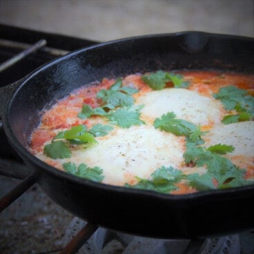 Looking across a cast iron skillet with poached eggs in a tomato sauce.