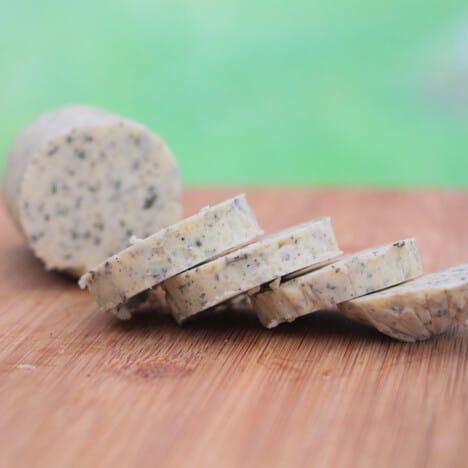 A roll of fresh herb butter on a wooden chopping board with some slices done ready to be served.