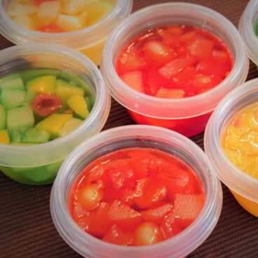 Small plastic Tupperware containers are filled with different colors of Jello and mixed fruits.