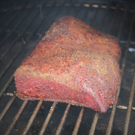 A rich mahogany red smoking brisket flat sitting on a grill grate.