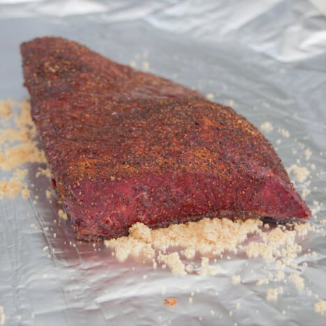 A sheet of foil with a partly smoked brisket flat sitting on brown sugar.