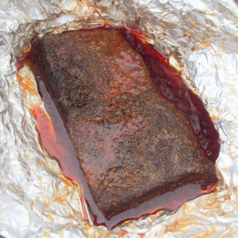 A smoked brisket flat sitting in foil and the liquids it was cooked in.