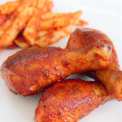 Three smoked and glazed chicken drumsticks on a white plate.